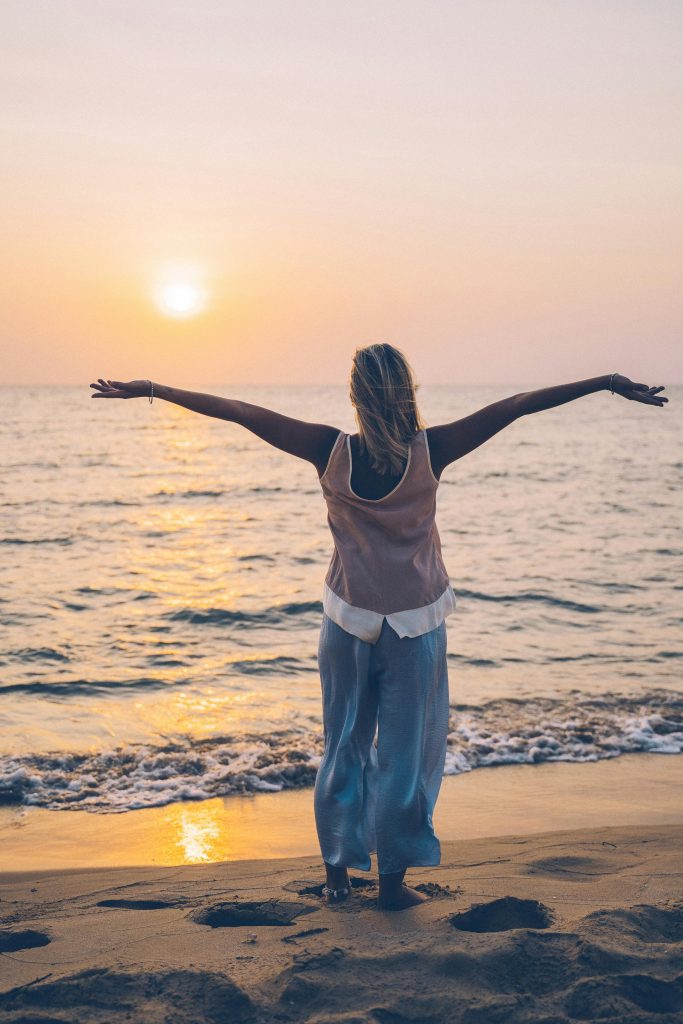 pexels-photo-6712299-6712299 Woman with arms extended enjoying a serene beach sunset, capturing tranquility and freedom.